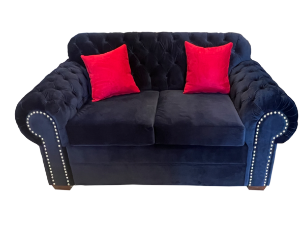 Royal Velvet Chesterfield Sofa in blue velvet with tufted design, nailhead trim, and red accent pillows.